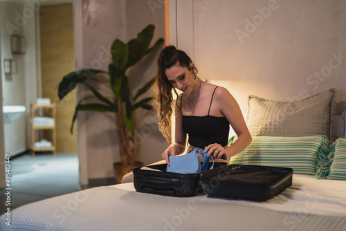 Chica joven delgada deshaciendo maleta sobre la cama de hotel