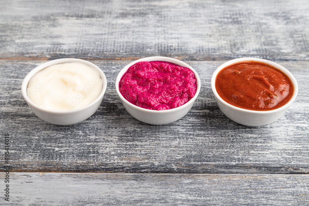 ceramic sauce bowls with horseradish, tomato sauce and mayonnaise on a gray. Side view, copy space. ceramic sauce bowls with horseradish, tomato sauce and mayonnaise on a gray. Side view, copy space.