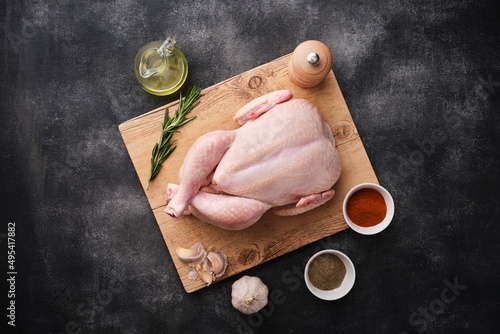 Whole raw chicken on wooden board on dark background. Preparing raw chicken. Top view.