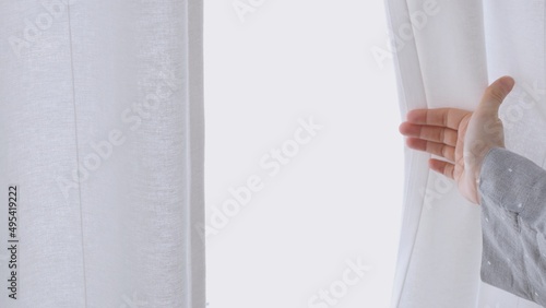 Close-up of hands reaching out to the curtains and opening the window, the light floods the room with bright light. In the morning open the curtains to let in daylight from the window.