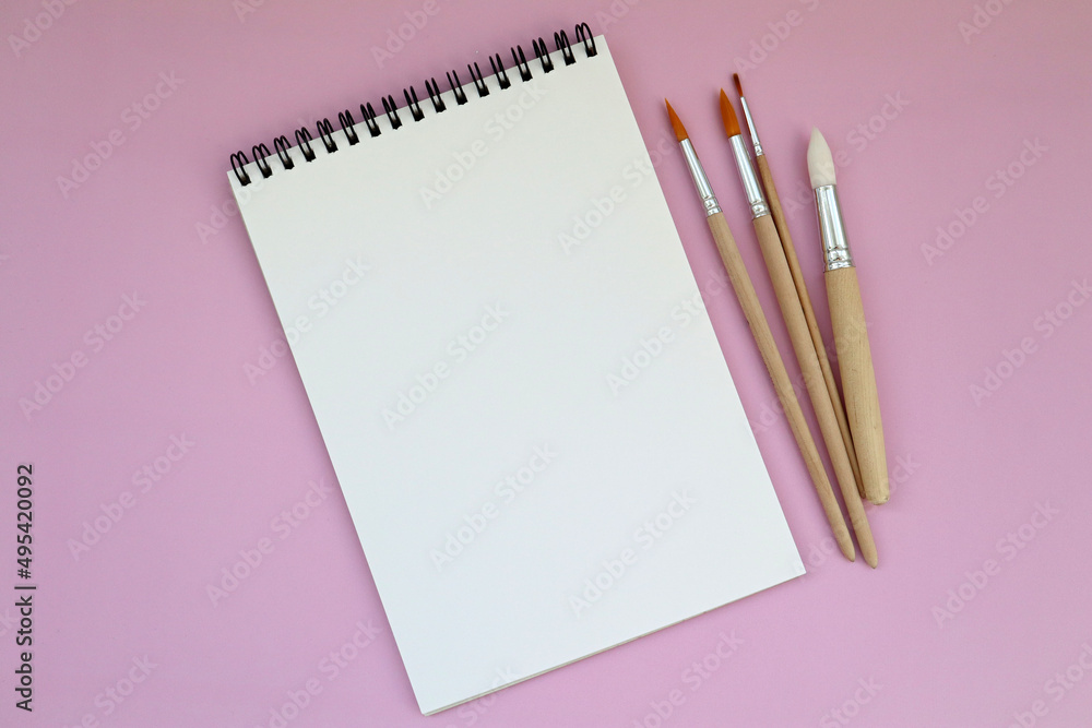 A clean white notebook and brushes on a pink background with space to copy. Layout, mockup space for text, drawing.