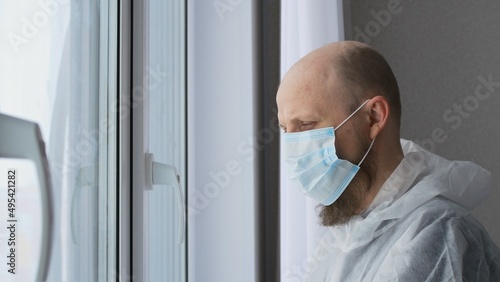 Doctors stand at the window adjusting the mask on his face. A man with a bald head is a laboratory assistant in a medical institution. Work in the hospital laboratory assistant biologist.