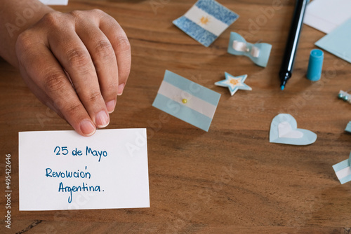 hand holding a piece of paper written in Spanish 25 de mayo revolucion Argentina, in the background colors of light blue and white