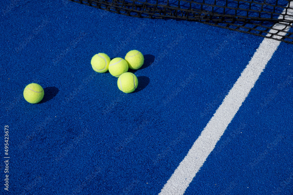 selective focus, five paddle tennis balls and the net of a blue paddle tennis court