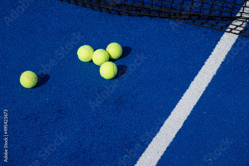 selective focus, five paddle tennis balls and the net of a blue paddle tennis court © Vic