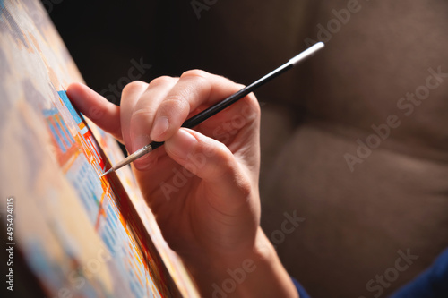 Close-up of a young female artist's hand with a thin brush painting a picture on canvas in a dark room. Shallow depth of field. high contrast