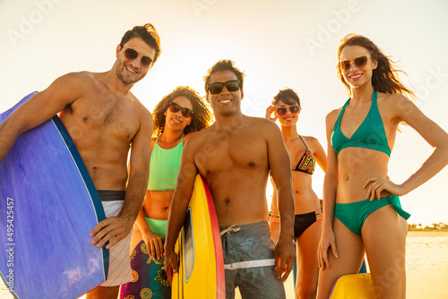 Smiling friends carrying bodyboards having fun on beach photo