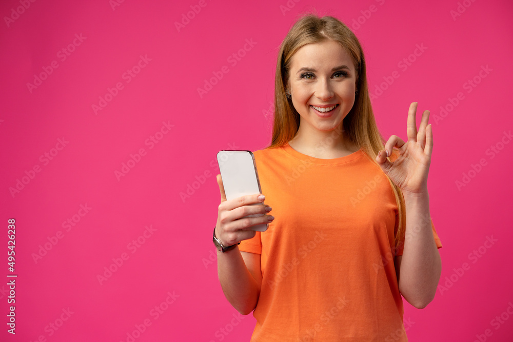 Young smiling woman holding smartphone and showiing OK sign Young smiling woman holding smartphone and showiing OK sign