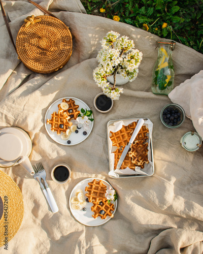 Breakfast picnic with waffles and tea in spring blossom garden on a white tablecloth on a sunny day, cherry blossoms. Outdoor, picnic, brunch, spring mood