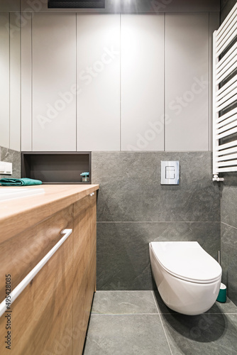 Łazienka z umywalką, baterią, dużym lustrem oraz kabiną prysznicową. Toaleta w mieszkaniu. Kolory szarości i drewno