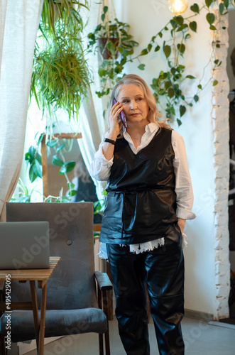 Elderly business woman stands in a cafe and talks on the phone