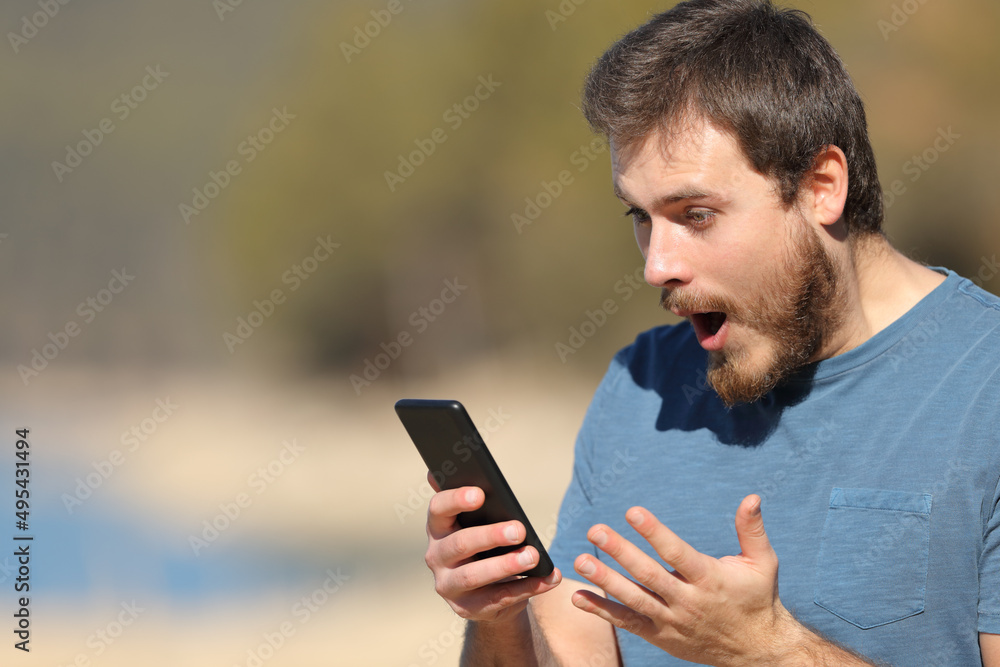Shocked man checking smart phone in nature Shocked man checking smart phone in nature