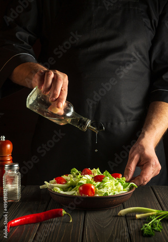 Chef pours oil into a salad bowl in the kitchen. Cooking delicious and healthy food with a set of vitamins