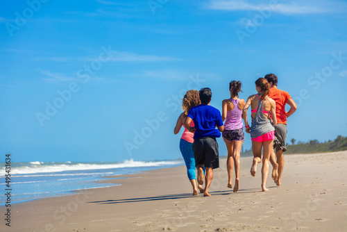 Healthy young friends jogging barefoot by the ocean