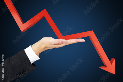 Businessman hand holding falling red chart arrow on dark blue background. Crisis and fall concept.