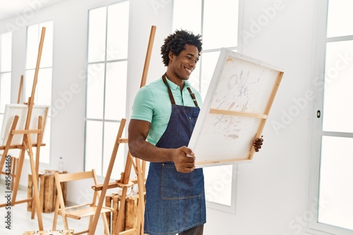 Young african american artist man smiling happy holding canvas at art studio.