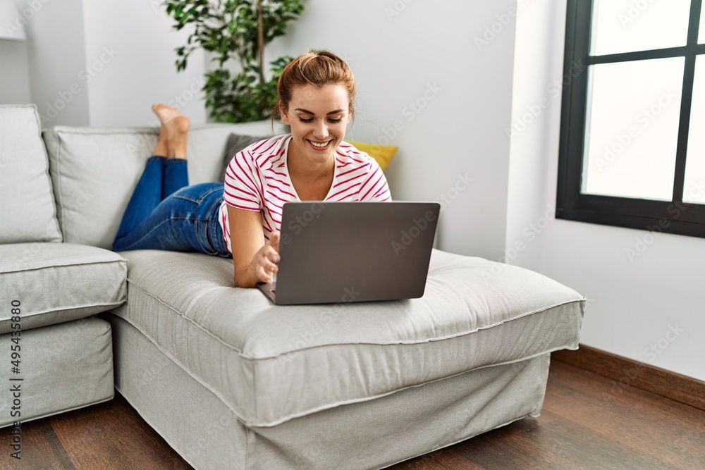 Young woman using laptop lying on sofa at home Young woman using laptop lying on sofa at home