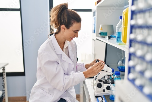 Young woman wearing scientist uniform using microscope at laboratory
