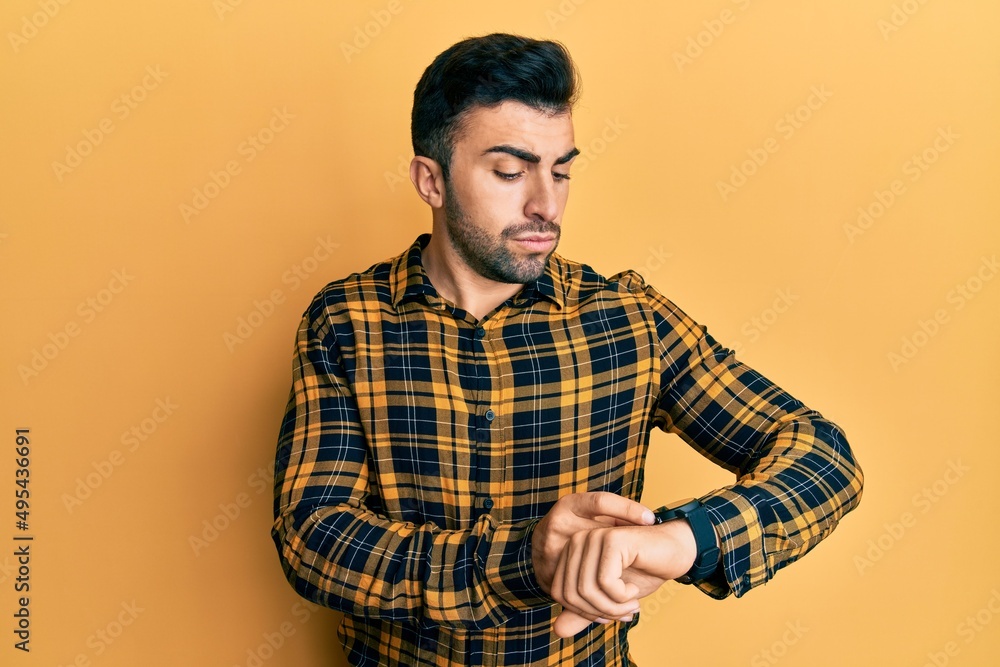 Young hispanic man wearing casual clothes checking the time on wrist watch, relaxed and confident Young hispanic man wearing casual clothes checking the time on wrist watch, relaxed and confident