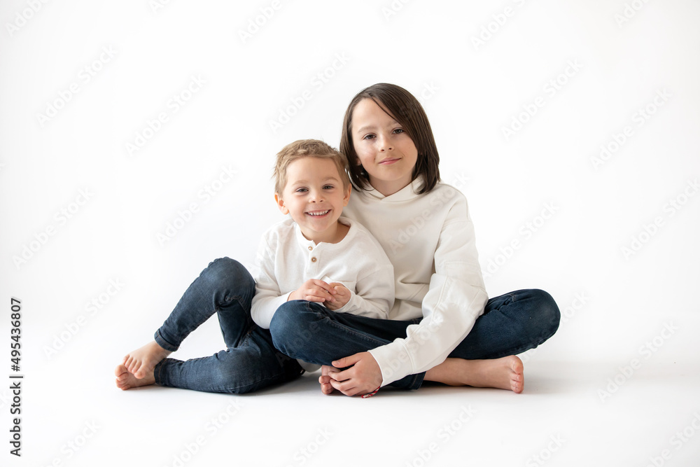 Cute stylish toddler child and older brother, boys with white shirts on white background, family kids portrait Cute stylish toddler child and older brother, boys with white shirts on white background, family kids portrait