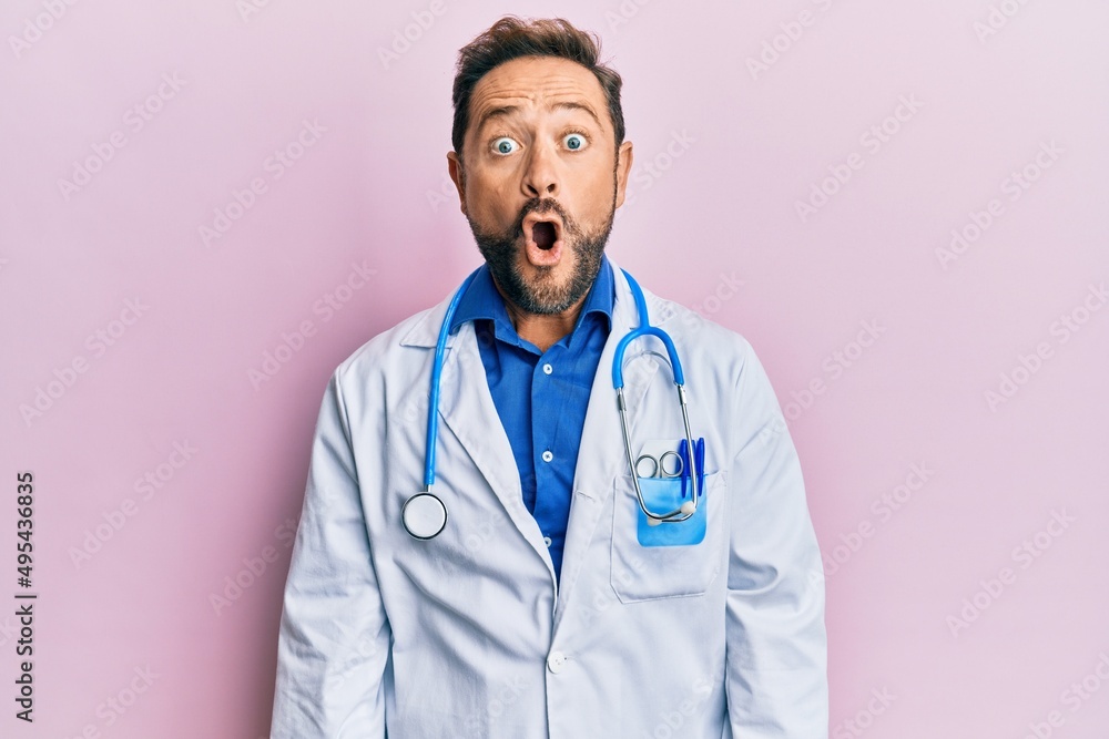Middle age man wearing doctor uniform and stethoscope scared and amazed with open mouth for surprise, disbelief face Middle age man wearing doctor uniform and stethoscope scared and amazed with open mouth for surprise, disbelief face