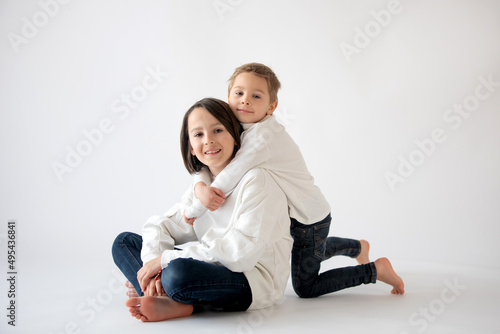 Cute stylish toddler child and older brother, boys with white shirts on white background, family kids portrait