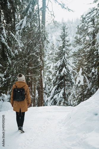 Back view of woman in brown coat standing on snow covered ground near trees