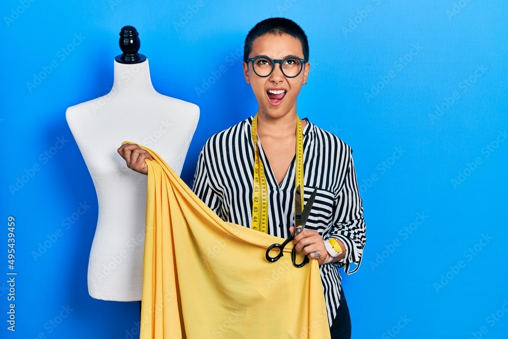 Beautiful hispanic woman with short hair standing by manikin holding cloth angry and mad screaming frustrated and furious, shouting with anger looking up.