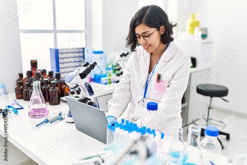 Young latin woman wearing scientist uniform using laptop working at laboratory