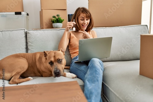 Young caucasian woman having video call and holding key sitting on sofa with dog at home