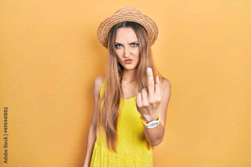 Young blonde girl wearing summer hat showing middle finger, impolite and rude fuck off expression Young blonde girl wearing summer hat showing middle finger, impolite and rude fuck off expression