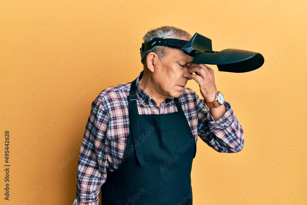 Handsome senior man with grey hair wearing welding protection mask tired rubbing nose and eyes feeling fatigue and headache. stress and frustration concept. Handsome senior man with grey hair wearing welding protection mask tired rubbing nose and eyes feeling fatigue and headache. stress and frustration concept.