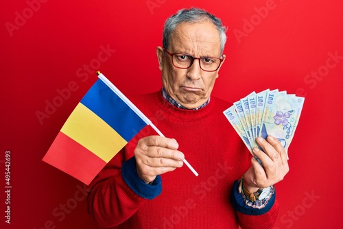 Handsome senior man with grey hair holding romania flag and leu banknotes skeptic and nervous, frowning upset because of problem. negative person.