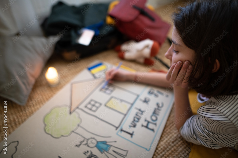 Sad Ukrainian refugee child missing her home and drawing her family. Ukrainian war concept. Sad Ukrainian refugee child missing her home and drawing her family. Ukrainian war concept.