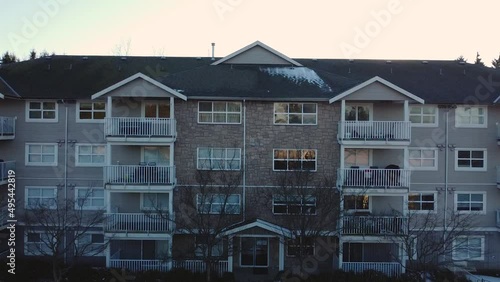 Front face of a four story condo building is Whalley Surrey BC City neighbourhood Aerial medium wide ascending revealing sunflare tall buildings towers constructuction on distance bright day blue sky photo