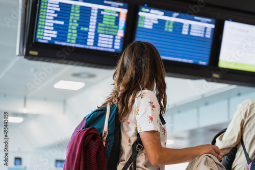 Back view unrecognizable woman reading flights information on departures board at international airport.