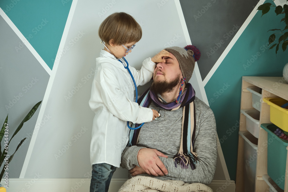 Obraz premium Father and child playing clinic and doctor, little boy in medical gown with stethoscope treats dad