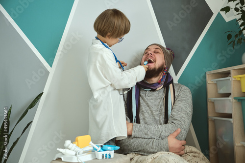 Father and child playing clinic and doctor  little boy dentist in medical gown with stethoscope treats dad