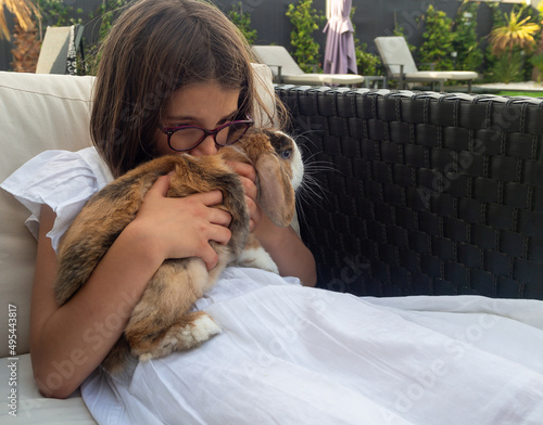 Portrait of girl with eyeglasses kissing a French lop rabbit while holding it in her arms