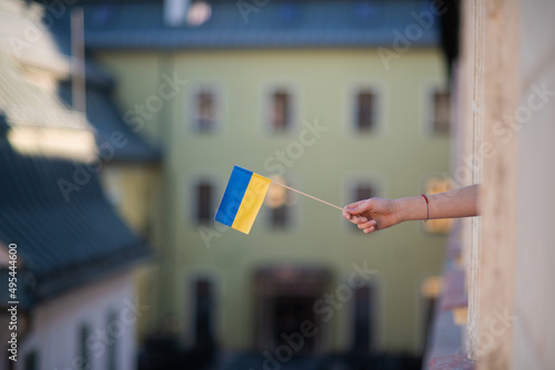Girl's hand sticking Ukrainian flag out from window solidarity with Ukraine in war concept.