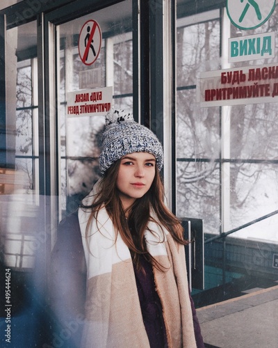 Portrait of woman wearing knit hat and scarf standing by glass doors