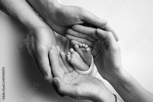 The palms of the father, the mother are holding the foot of the newborn baby. Feet of the newborn on the palms of the parents. Studio photography of a child's toes, heels and feet. Black white.