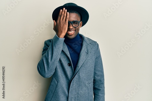 Young african american man wearing elegant style covering one eye with hand, confident smile on face and surprise emotion.