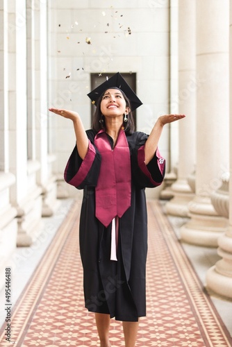 Smiling young Asian-American woman in graduation dress throwing confetti photo