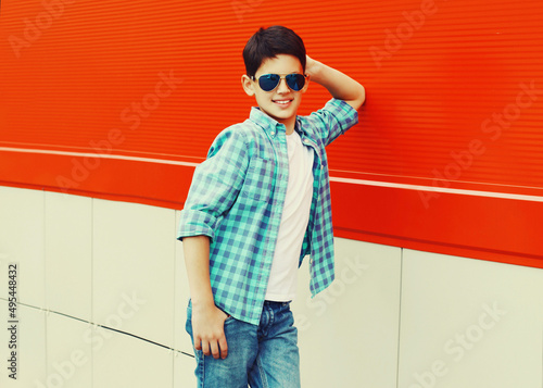Portrait of teenager boy wearing sunglasses and shirt in the city on red background