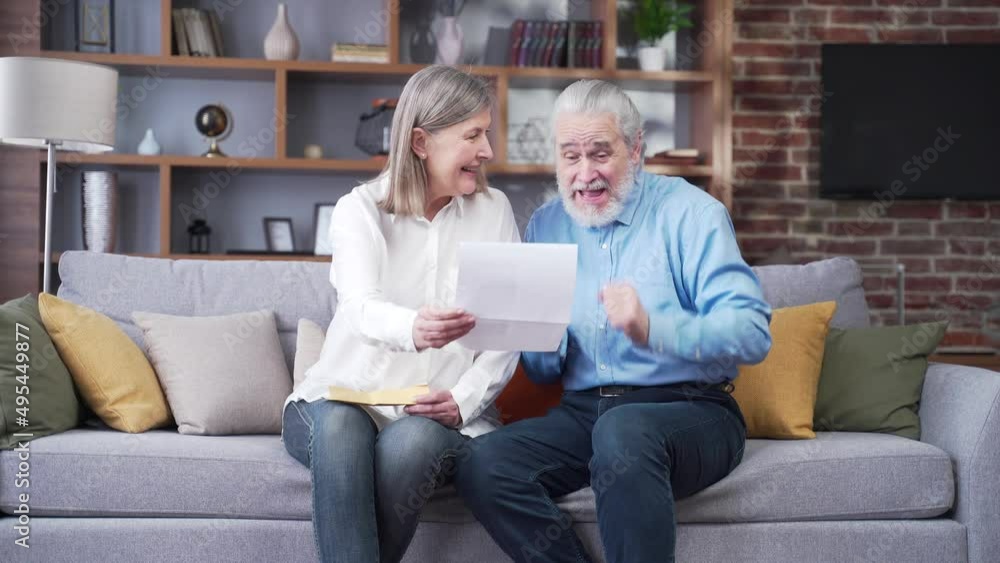 Senior gray haired family member receiving letter or document rejoicing sitting at home. Cheerful husband and wife retirees smiling while reading the good news. Old people watch. Joyful grandparents Senior gray haired family member receiving letter or document rejoicing sitting at home. Cheerful husband and wife retirees smiling while reading the good news. Old people watch. Joyful grandparents