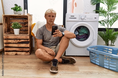 Fotografia Young blond man doing laundry using smartphone depressed and worry for distress, crying angry and afraid