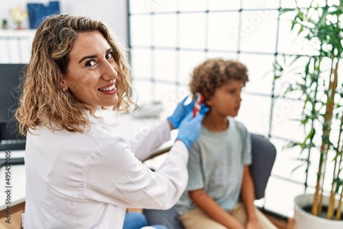 Mother and son wearing doctor uniform examining ear using otoscope at clinic