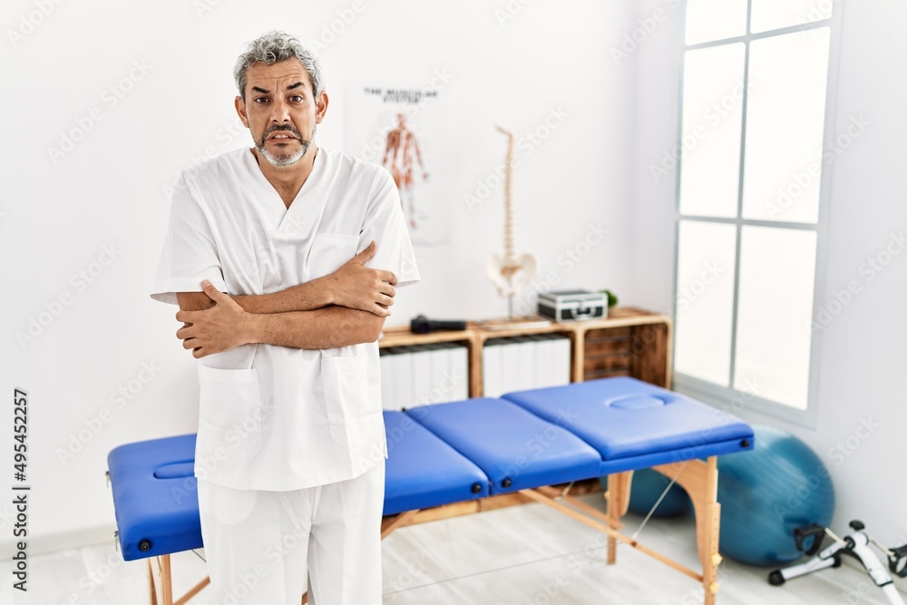 Middle age hispanic therapist man working at pain recovery clinic shaking and freezing for winter cold with sad and shock expression on face Middle age hispanic therapist man working at pain recovery clinic shaking and freezing for winter cold with sad and shock expression on face