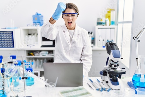 Young hispanic woman wearing scientist uniform working at laboratory annoyed and frustrated shouting with anger, yelling crazy with anger and hand raised
